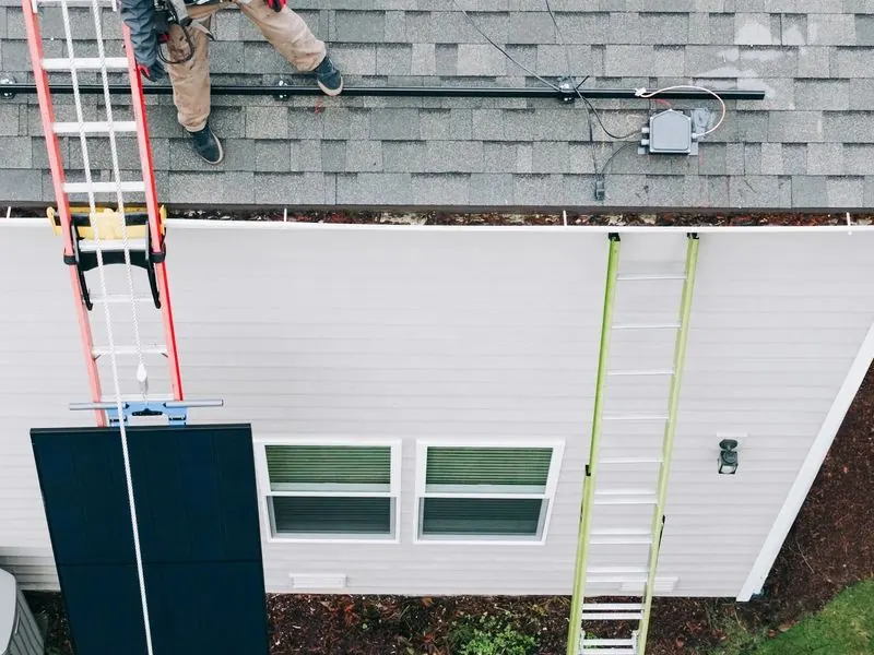 Roofer on a ladder installing new architectural shingles during a roof replacement in Lake Havasu City